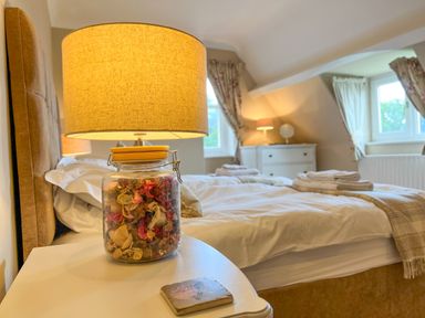 A bedroom with a bed, bedside table with a lamp and jar of dried flowers at Geltsdale East Wing in Wetheral