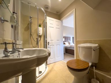 A bathroom with a sink shower and toilet visible with an open door showing a bedroom at Geltsdale East Wing in Wetheral