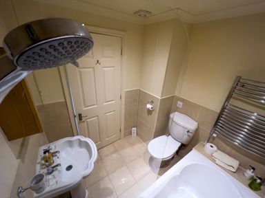A bathroom with a white sink, toilet, bathtub, and a door at Geltsdale East Wing in Wetheral