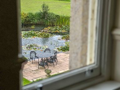 A metal table and chairs on a stone patio near a pond with lily pads and plants at Geltsdale East Wing in Wetheral