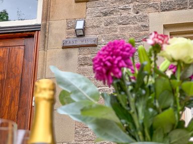A close-up of flowers with a stone building wall and a wooden door in the background at Geltsdale East Wing in Wetheral