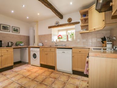 A kitchen with wooden cabinets a washing machine dishwasher and a window with plants and plates on the wall at Springarth Cottage in Newby