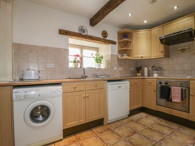 A kitchen with wooden cabinets a washing machine a dishwasher an oven and a window with plants at Springarth Cottage in Newby