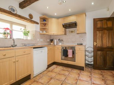 A kitchen with wooden cabinets tiled floor dishwasher oven and a dark wooden door at Springarth Cottage in Newby