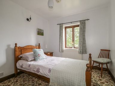 A bedroom with a wooden bed a bedside table a chair and a window with curtains at Springarth Cottage in Newby