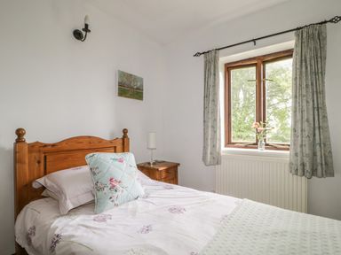 A bedroom with a wooden bed a bedside table and a window with curtains at Springarth Cottage in Newby