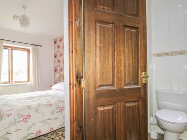 A bedroom with a floral bedspread and window next to a bathroom with a toilet at Springarth Cottage in Newby