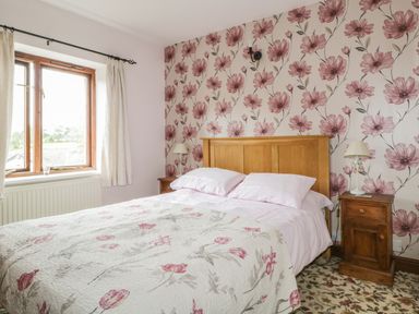 A bedroom with a wooden bed frame floral wallpaper and two bedside tables with lamps at Springarth Cottage in Newby