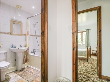 A bathroom with a toilet sink and bathtub next to a bedroom with a bed and chair at Springarth Cottage in Newby