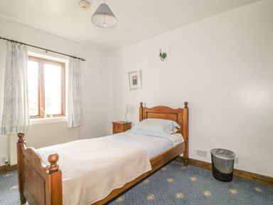 A bedroom with a wooden single bed a bedside table with a lamp a window with curtains and a waste bin at Springarth Cottage in Newby