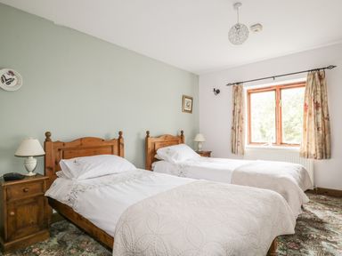 A bedroom with two single wooden beds with white bedding wooden bedside tables and a window at Springarth Cottage in Newby
