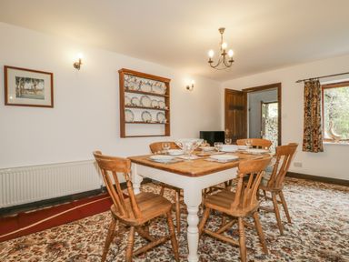 A dining room with a wooden table set for six and a wooden plate rack on the wall at Springarth Cottage in Newby