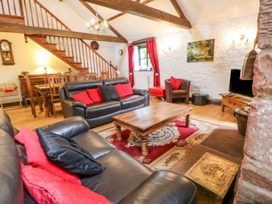 A living room with leather sofas wooden coffee table red and black cushions and wooden staircase at The Old Byre in Appleby-in-Westmorland