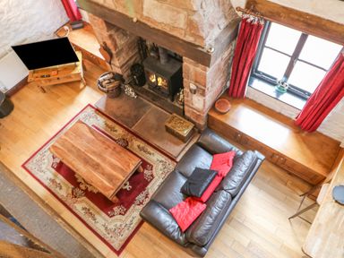 A living room with a leather sofa red cushions wooden coffee table fireplace and television at The Old Byre in Appleby-in-Westmorland