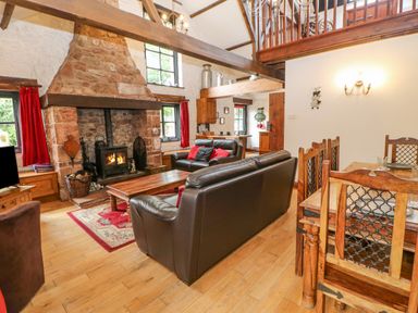 A living room with a stone fireplace leather sofas and a wooden dining table at The Old Byre in Appleby-in-Westmorland