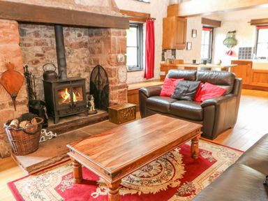 A living room with a wood burning stove a wooden coffee table and leather sofas at The Old Byre in Appleby-in-Westmorland
