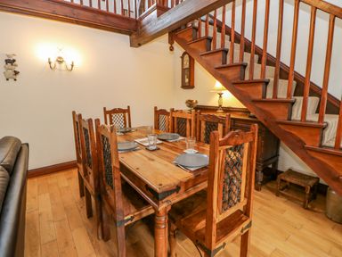 A dining area with a wooden table set with plates and glasses under a wooden staircase at The Old Byre in Appleby-in-Westmorland