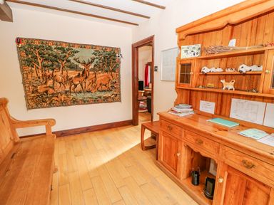 A room with wooden furniture including a bench and a cabinet with shelves and drawers a tapestry with deer hangs on the wall at The Old Byre in Appleby-in-Westmorland