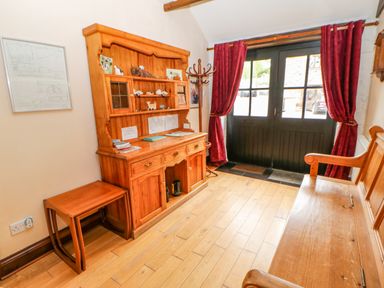 An entryway with wooden bench and hutch with decorations and red curtains at The Old Byre in Appleby-in-Westmorland