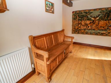 A wooden bench against a wall with a radiator and two animal paintings on the walls at The Old Byre in Appleby-in-Westmorland