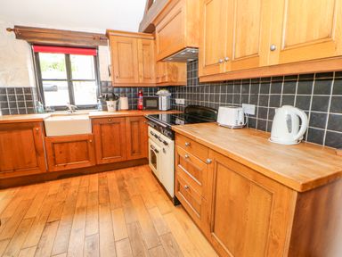 A kitchen with wooden cabinets black tiled backsplash and wooden floor at The Old Byre in Appleby-in-Westmorland