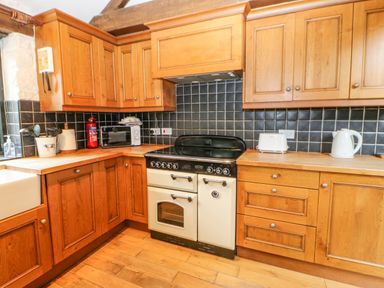 A kitchen with wooden cabinets black tiled backsplash and appliances including a stove microwave kettle and toaster at The Old Byre in Appleby-in-Westmorland