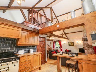 A kitchen with wooden cabinets and a black tiled backsplash connected to a living area with sofas and red curtains at The Old Byre in Appleby-in-Westmorland