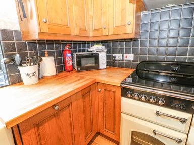 A kitchen corner with wooden cabinets a microwave a fire extinguisher cooking utensils and a stove at The Old Byre in Appleby-in-Westmorland