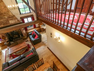 A living room with black sofas and red pillows near a stone fireplace and wooden coffee table at The Old Byre in Appleby-in-Westmorland
