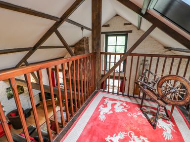 A loft area with wooden railing a spinning wheel and a red carpet with dragon designs at The Old Byre in Appleby-in-Westmorland