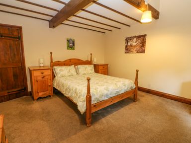 A bedroom with a wooden double bed two bedside tables table lamps and framed pictures on the wall at The Old Byre in Appleby-in-Westmorland