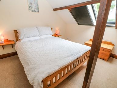 A bedroom with a wooden bed frame and white bedding with bedside tables and lamps at The Old Byre in Appleby-in-Westmorland