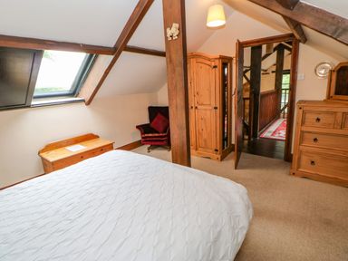 A bedroom with a bed chest armchair and wooden wardrobe at The Old Byre in Appleby-in-Westmorland