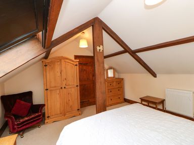 A bedroom with a bed a wooden wardrobe a chair radiator and a wooden dresser at The Old Byre in Appleby-in-Westmorland