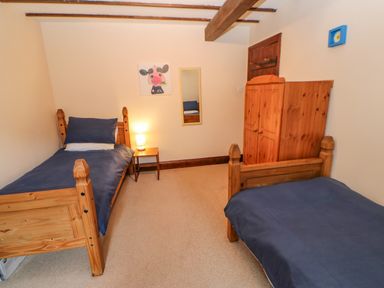 A bedroom with two single wooden beds a small table with a lamp a wooden wardrobe and a cow painting on the wall at The Old Byre in Appleby-in-Westmorland