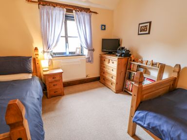 A bedroom with two wooden beds blue bedding a wooden dresser and bookshelf with TV at The Old Byre in Appleby-in-Westmorland
