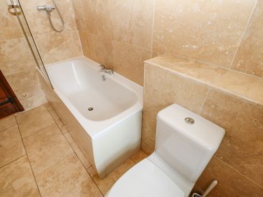 A bathroom with a bathtub and a toilet next to beige tiled walls and floor at The Old Byre in Appleby-in-Westmorland