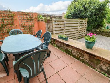 An outdoor patio with a plastic table and chairs potted plants and a wooden gate at The Old Byre in Appleby-in-Westmorland