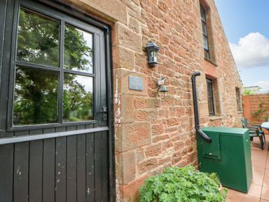 Exterior view of a stone building with a black door green utility box outdoor light and patio furniture at The Old Byre in Appleby-in-Westmorland