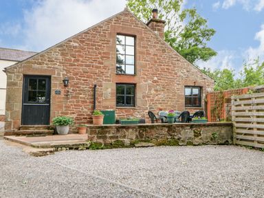 A stone cottage with a black door and windows a patio with potted plants and outdoor furniture at The Old Byre in Appleby-in-Westmorland