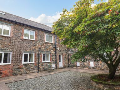 A stone courtyard with a tree in a raised stone planter and patio furniture at Maple Cottage in Keswick