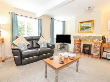 A living room with a black leather sofa a wooden coffee table and a TV by a brick fireplace at Maple Cottage in Keswick