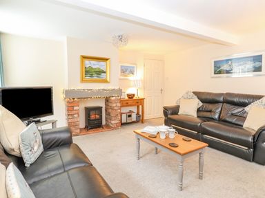 A living room with black leather sofas a coffee table and a fireplace with brick surround at Maple Cottage in Keswick