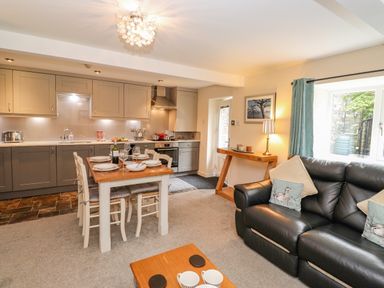 An open plan kitchen and living room with dining table set and black leather sofa at Maple Cottage in Keswick