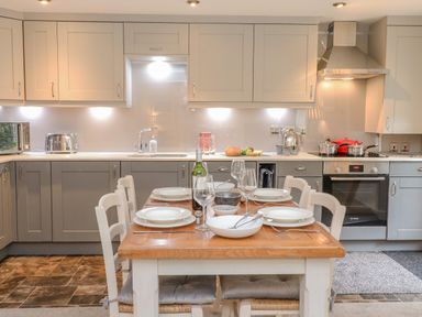 A kitchen with a wooden dining table set for four with plates and glasses at Maple Cottage in Keswick