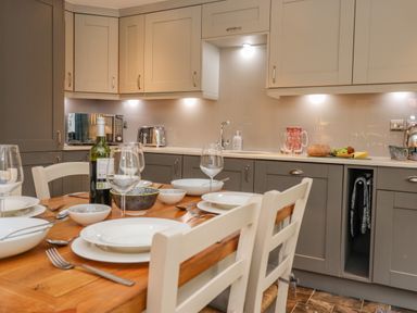 A kitchen with a wooden dining table set with plates glasses and a bottle of wine at Maple Cottage in Keswick