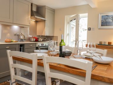 A kitchen with a wooden dining table set with plates glasses and a bottle of wine at Maple Cottage in Keswick