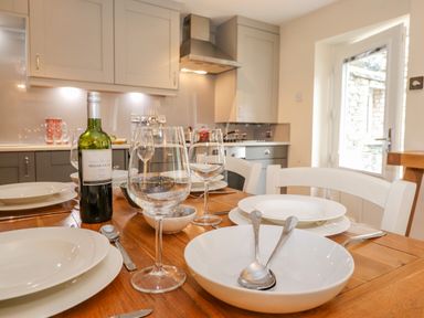 A kitchen with a wooden dining table set with white plates wine glasses and a bottle of wine at Maple Cottage in Keswick