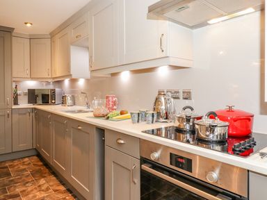 A kitchen with gray cabinets a stovetop with pots a toaster kettle microwave and a countertop with cups bread and fruit at Maple Cottage in Keswick