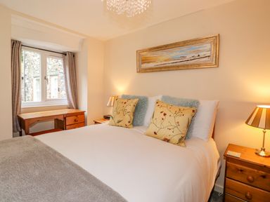 A bedroom with a bed two pillows two bedside tables with lamps a wooden desk and a window at Maple Cottage in Keswick